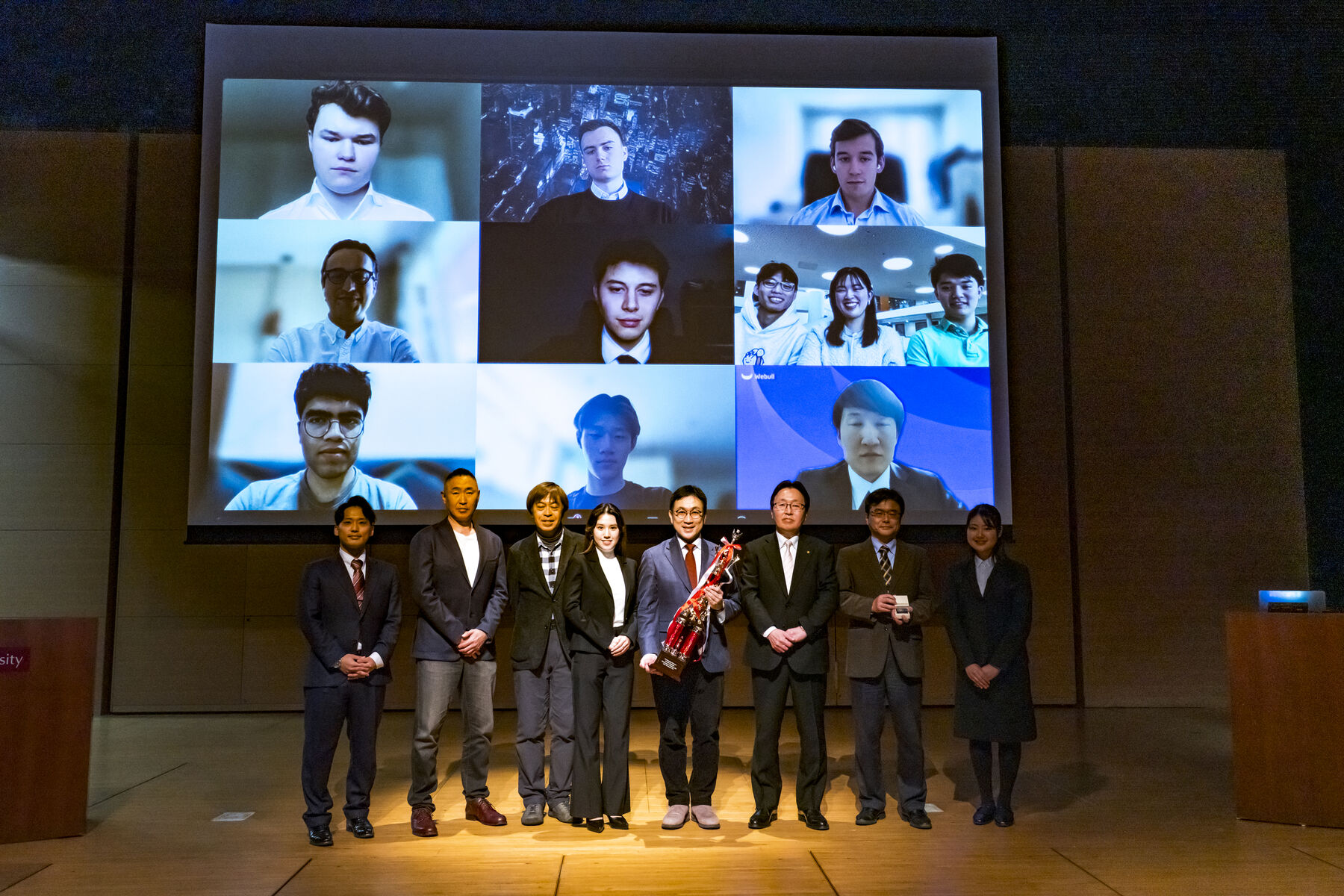 Judges and organizers on stage at the WIC2025 closing ceremony, with teams joining on screen